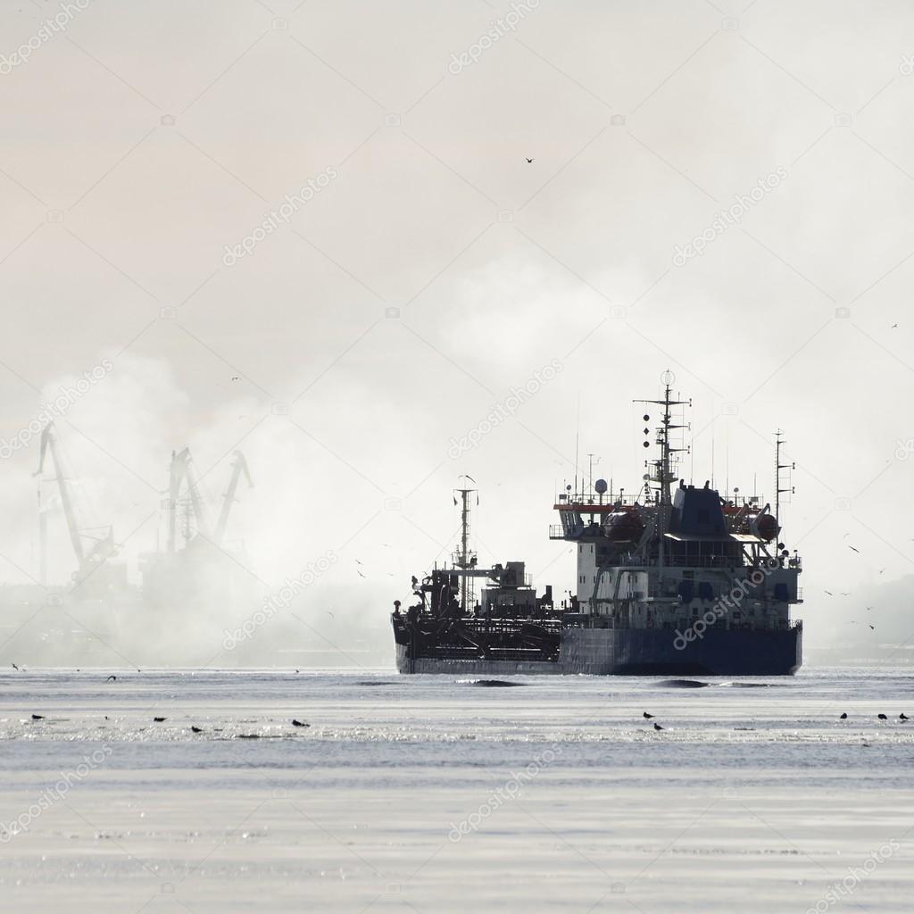 Silhouettes of cargo ship and port cranes in fog