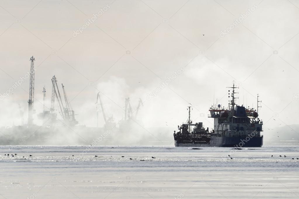 Silhouettes of cargo ship and port cranes in fog