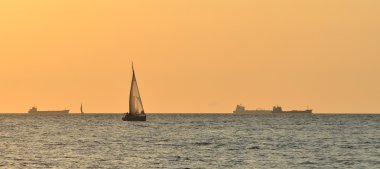 karşı büyük kargo gemisi günbatımında yelkenli yat