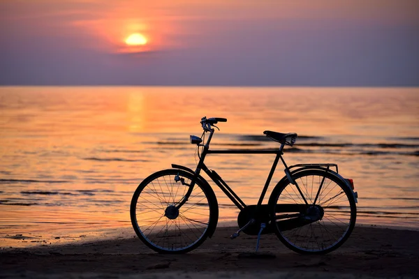 Старый винтажный велосипед на пляже против заката в море — стоковое фото