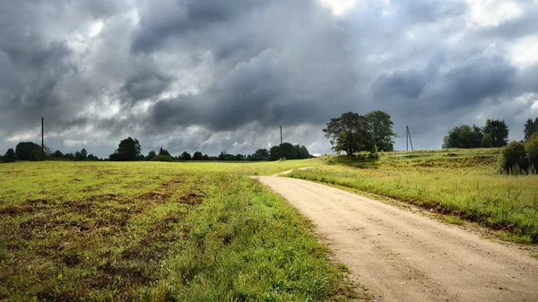 Campo verde e a estrada contra o céu tempestuoso — Fotografia de Stock