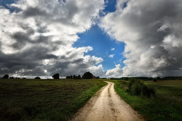 Grüne Wiese und die Straße gegen stürmischen Himmel — Stockfoto
