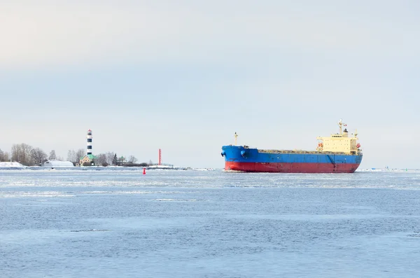 Cargo ship entering port with lighthouse at the background — Zdjęcie stockowe