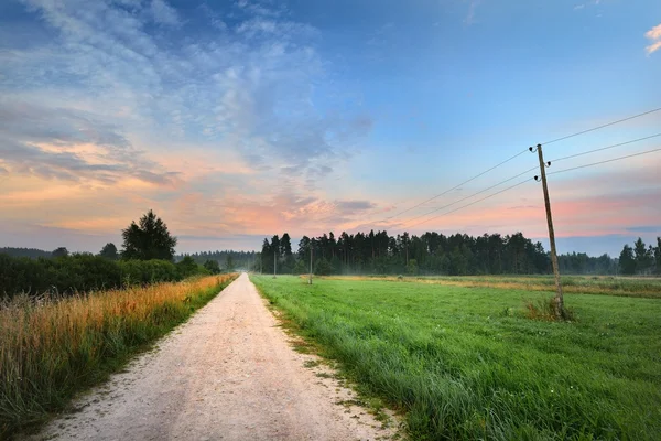 Nascer do sol no campo com uma estrada rural — Fotografia de Stock