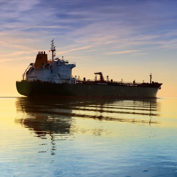 Cargo ship sailing away against colorful sunset — Stock Photo, Image