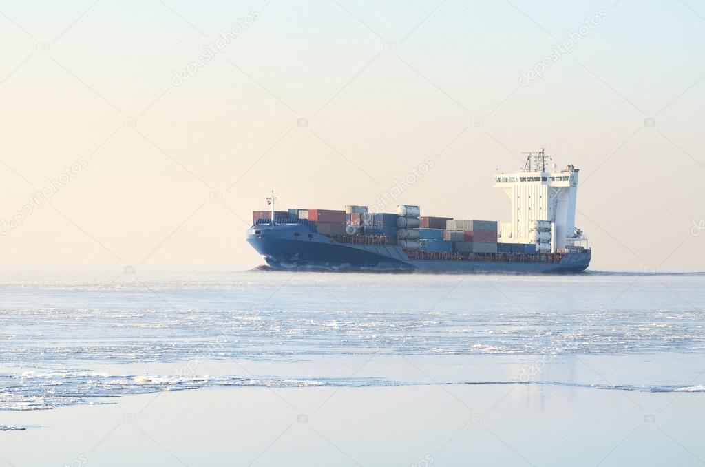 Cargo container ship sailing in still frozen winter sea