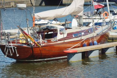 Yat limanındaki bir rıhtıma demirlemiş ahşap meşe güverteli zarif bir modern yelkenli tekne. Deniz aracı, ulaşım, spor, yelkenli yarışı, dinlenme, boş zaman aktivitesi, gezi, tatiller, yaşam tarzı temaları