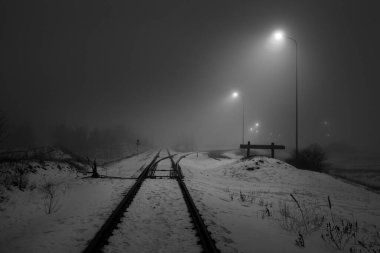 Geceleri karla kaplı demiryolu aydınlanıyor. Atmosferik kış manzarası. Siyah beyaz görüntü. Boşluk, sessizlik, yalnızlık kavramları.