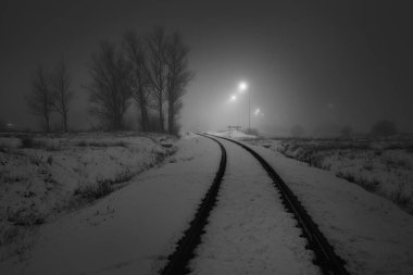 Geceleri karla kaplı demiryolu aydınlanıyor. Atmosferik kış manzarası. Siyah beyaz görüntü. Boşluk, sessizlik, yalnızlık kavramları.