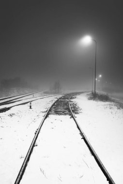Geceleri karla kaplı demiryolu aydınlanıyor. Atmosferik kış manzarası. Siyah beyaz görüntü. Boşluk, sessizlik, yalnızlık kavramları.