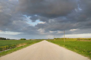 Fırtınadan sonra tarladan geçen boş köy yolu. Arabadan bir manzara. Idyllic kırsal kesim. Renkli, parlayan günbatımı bulutları. Ulaşım, yolculuk, özgürlük, seyahat tutkusu, uzak yerler kavramları.