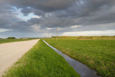 Fırtınadan sonra tarladan geçen boş köy yolu. Arabadan bir manzara. Idyllic kırsal kesim. Renkli, parlayan günbatımı bulutları. Ulaşım, yolculuk, özgürlük, seyahat tutkusu, uzak yerler kavramları.