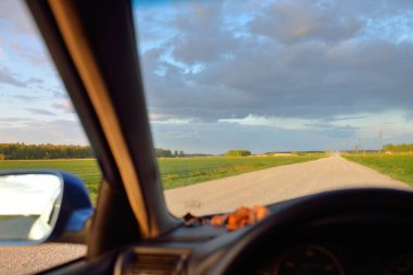 Fırtınadan sonra tarladan geçen boş köy yolu. Arabadan bir manzara. Idyllic kırsal kesim. Renkli, parlayan günbatımı bulutları. Ulaşım, yolculuk, özgürlük, seyahat tutkusu, uzak yerler kavramları.