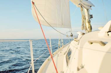 Gün batımında açık denizde yelkenli yelkenli yelkenli. Gökyüzü açık. Güverteden pruvaya bir manzara, direk, yelkenler. Ulaşım, seyahat, gezi, spor, eğlence, boş zaman aktivitesi, yarış, yelkenli yarışı