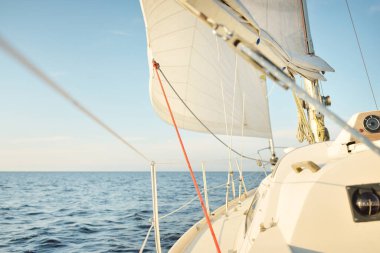 Gün batımında açık denizde yelkenli yelkenli yelkenli. Gökyüzü açık. Güverteden pruvaya bir manzara, direk, yelkenler. Ulaşım, seyahat, gezi, spor, eğlence, boş zaman aktivitesi, yarış, yelkenli yarışı