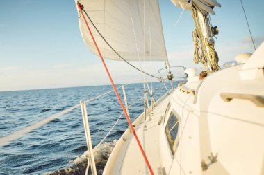 Gün batımında açık denizde yelkenli yelkenli yelkenli. Gökyüzü açık. Güverteden pruvaya bir manzara, direk, yelkenler. Ulaşım, seyahat, gezi, spor, eğlence, boş zaman aktivitesi, yarış, yelkenli yarışı