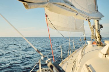 Gün batımında açık denizde yelkenli yelkenli yelkenli. Gökyüzü açık. Güverteden pruvaya bir manzara, direk, yelkenler. Ulaşım, seyahat, gezi, spor, eğlence, boş zaman aktivitesi, yarış, yelkenli yarışı