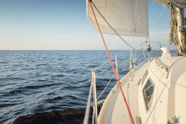 Gün batımında açık denizde yelkenli yelkenli yelkenli. Gökyüzü açık. Güverteden pruvaya bir manzara, direk, yelkenler. Ulaşım, seyahat, gezi, spor, eğlence, boş zaman aktivitesi, yarış, yelkenli yarışı