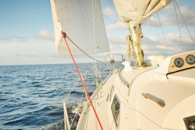 Gün batımında açık denizde yelkenli yelkenli yelkenli. Gökyüzü açık. Güverteden pruvaya bir manzara, direk, yelkenler. Ulaşım, seyahat, gezi, spor, eğlence, boş zaman aktivitesi, yarış, yelkenli yarışı