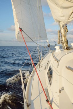 Gün batımında açık denizde yelkenli yelkenli yelkenli. Gökyüzü açık. Güverteden pruvaya bir manzara, direk, yelkenler. Ulaşım, seyahat, gezi, spor, eğlence, boş zaman aktivitesi, yarış, yelkenli yarışı