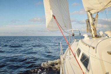 Gün batımında açık denizde yelkenli yelkenli yelkenli. Gökyüzü açık. Güverteden pruvaya bir manzara, direk, yelkenler. Ulaşım, seyahat, gezi, spor, eğlence, boş zaman aktivitesi, yarış, yelkenli yarışı