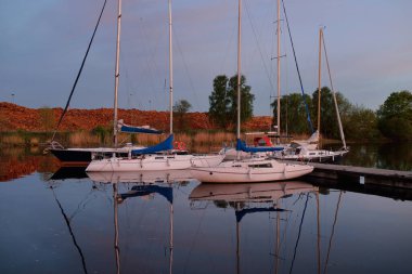 Günbatımında yat limanında demirlemiş zarif ve modern yelkenliler. Dramatik gökyüzü, parlayan altın bulutlar. Tatiller, ulaşım, spor, eğlence, turizm, seyahat, liman