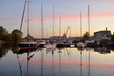 Günbatımında yat limanında demirlemiş zarif ve modern yelkenliler. Dramatik gökyüzü, parlayan altın bulutlar. Tatiller, ulaşım, spor, eğlence, turizm, seyahat, liman