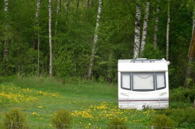 Beyaz karavan, kamp alanındaki yeşil bir orman çimenliğinde. Avrupa. Yaz manzarası. Yaşam tarzı, seyahat, eko-turizm, yol gezisi, yolculuk, tatiller, eğlence, ulaşım, karavan, karavan