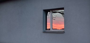 Ağaç dalları ve parlayan kırmızı bulutlar, pencere camındaki yansımalar. Kış batımı. Manzara kavramı. Dış bina, uzak yerler, çevre koruma kavramları. Panoramik resim