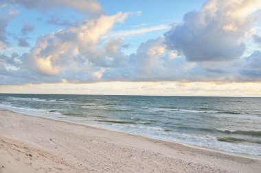 Fırtınadan sonra Baltık kıyıları (kum tepeleri, plaj). Gün batımı, yumuşak altın güneş ışığı, parlayan bulutlar. Resimli panoramik manzara. Doğa, çevre, ekoloji, eko-turizm, yürüyüş, keşif kavramları
