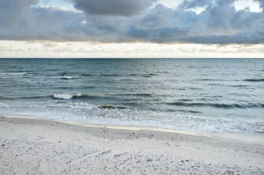 Fırtınadan sonra Baltık kıyıları (kum tepeleri, plaj). Gün batımı, yumuşak altın güneş ışığı, parlayan bulutlar. Resimli panoramik manzara. Doğa, çevre, ekoloji, eko-turizm, yürüyüş, keşif kavramları