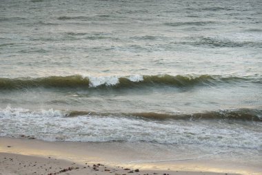 Fırtınadan sonra Baltık kıyıları. Gün batımı, yumuşak altın güneş ışığı. Su yüzeyi dokusu, çarpan dalgalar ve sıçramalar. Resimli panoramik manzara, arka plan. Doğa, çevre, ekoloji kavramları
