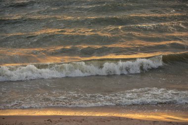Fırtınadan sonra Baltık kıyıları. Gün batımı, yumuşak altın güneş ışığı. Su yüzeyi dokusu, çarpan dalgalar ve sıçramalar. Resimli panoramik manzara, arka plan. Doğa, çevre, ekoloji kavramları