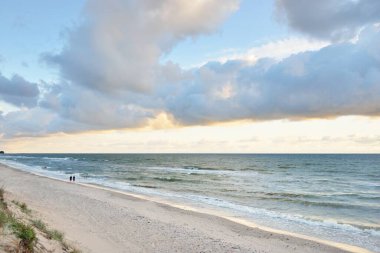 Fırtınadan sonra Baltık kıyıları (kum tepeleri, plaj). Gün batımı, yumuşak altın güneş ışığı, parlayan bulutlar. Resimli panoramik manzara. Doğa, çevre, ekoloji, eko-turizm, yürüyüş, keşif kavramları