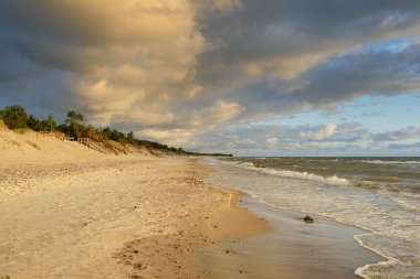 Fırtınadan sonra Baltık kıyıları (kum tepeleri, plaj). Gün batımı, yumuşak altın güneş ışığı, parlayan bulutlar. Resimli panoramik manzara. Doğa, çevre, ekoloji, eko-turizm, yürüyüş, keşif kavramları