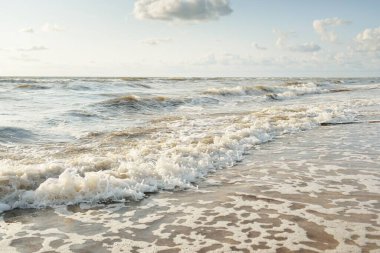 Fırtınadan sonra Baltık kıyıları. Gün batımı, yumuşak altın güneş ışığı. Su yüzeyi dokusu, çarpan dalgalar ve sıçramalar. Resimli panoramik manzara. Idyllic deniz manzarası. Doğa, çevre, ekoloji temaları