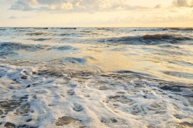 Fırtınadan sonra Baltık kıyıları. Gün batımı, yumuşak altın güneş ışığı. Su yüzeyi dokusu, çarpan dalgalar ve sıçramalar. Resimli panoramik manzara. Idyllic deniz manzarası. Doğa, çevre, ekoloji temaları
