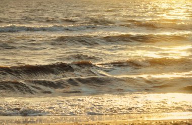 Fırtınadan sonra Baltık kıyıları. Gün batımı, yumuşak altın güneş ışığı. Su yüzeyi dokusu, çarpan dalgalar ve sıçramalar. Resimli panoramik manzara, arka plan. Doğa, çevre, ekoloji kavramları