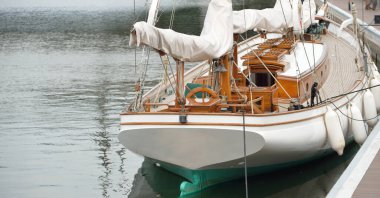 Yeni bir yat limanındaki iskeleye demirlenmiş pahalı bir retro yelkenli (ketch). Tahta meşe güvertesi, zarif detaylar. Ulaşım, denizcilik gemisi, tatiller, turizm, seyahat, yat yarışı, dinlenme