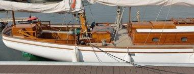 Yeni bir yat limanındaki iskeleye demirlenmiş pahalı bir retro yelkenli (ketch). Tahta meşe güvertesi, zarif detaylar. Ulaşım, denizcilik gemisi, tatiller, turizm, seyahat, yat yarışı, dinlenme