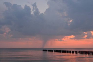 Fırtınadan sonra Baltık kıyılarından panoramik manzara. Dramatik gökyüzü, parlayan pembe günbatımı bulutları. Eski ahşap iskele. Doğa, çevre, ekoloji, iklim değişikliği, kararsız hava