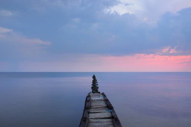 Fırtınadan sonra Baltık kıyılarından panoramik manzara. Dramatik gökyüzü, parlayan pembe günbatımı bulutları. Eski ahşap iskele. Doğa, çevre, ekoloji, iklim değişikliği, kararsız hava