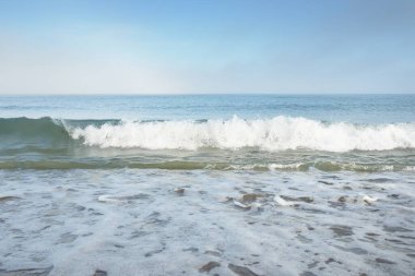 Güneş doğarken sisli bir havada Baltık Denizi kıyısından panoramik manzara. Dalgalar, sıçramalar, su yüzeyi. Yumuşak güneş ışığı, açık mavi gökyüzü. Idyllic yaz deniz manzarası. Saf doğa, çevre, ekoloji, eko-turizm