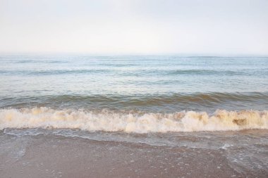 Güneş doğarken sisli bir havada Baltık Denizi kıyısından panoramik manzara. Dalgalar, sıçramalar, su yüzeyi. Yumuşak güneş ışığı, açık mavi gökyüzü. Idyllic yaz deniz manzarası. Saf doğa, çevre, ekoloji, eko-turizm