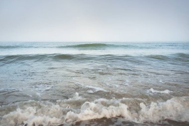 Güneş doğarken sisli bir havada Baltık Denizi kıyısından panoramik manzara. Dalgalar, sıçramalar, su yüzeyi. Yumuşak güneş ışığı, açık mavi gökyüzü. Idyllic yaz deniz manzarası. Saf doğa, çevre, ekoloji, eko-turizm