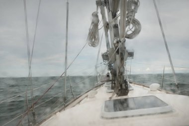 Fırtınada açık denizde yelken açan eski klasik bir yat. Tahta meşe güvertesi. Direğe ve yelkenlere bakın. Ketçap yelkenli. Dalgalar, su sıçramaları. Gezi, tatil, yelkenli yarışı, spor, boş zaman aktivitesi.