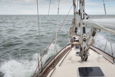 Fırtınada açık denizde yelken açan eski klasik bir yat. Tahta meşe güvertesi. Direğe ve yelkenlere bakın. Ketçap yelkenli. Dalgalar, su sıçramaları. Gezi, tatil, yelkenli yarışı, spor, boş zaman aktivitesi.