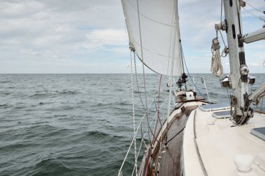 Fırtınada açık denizde yelken açan eski klasik bir yat. Tahta meşe güvertesi. Direğe ve yelkenlere bakın. Ketçap yelkenli. Dalgalar, su sıçramaları. Gezi, tatil, yelkenli yarışı, spor, boş zaman aktivitesi.