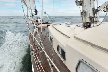 Fırtınada açık denizde yelken açan eski klasik bir yat. Tahta meşe güvertesi. Direğe ve yelkenlere bakın. Ketçap yelkenli. Dalgalar, su sıçramaları. Gezi, tatil, yelkenli yarışı, spor, boş zaman aktivitesi.