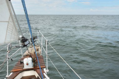 Fırtınada açık denizde yelken açan eski klasik bir yat. Tahta meşe güvertesi. Direğe ve yelkenlere bakın. Ketçap yelkenli. Dalgalar, su sıçramaları. Gezi, tatil, yelkenli yarışı, spor, boş zaman aktivitesi.